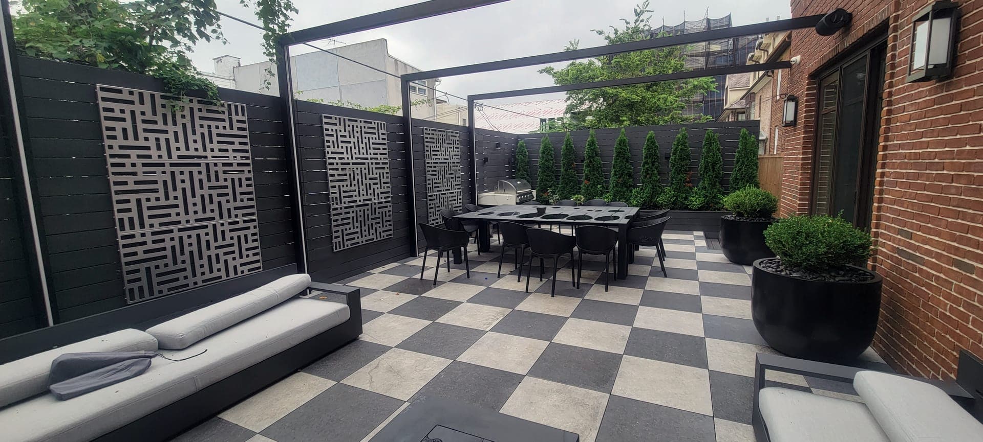 A finished MintScapes backyard with checkerboard pavers, a black steel pergola, and laser-cut privacy screens