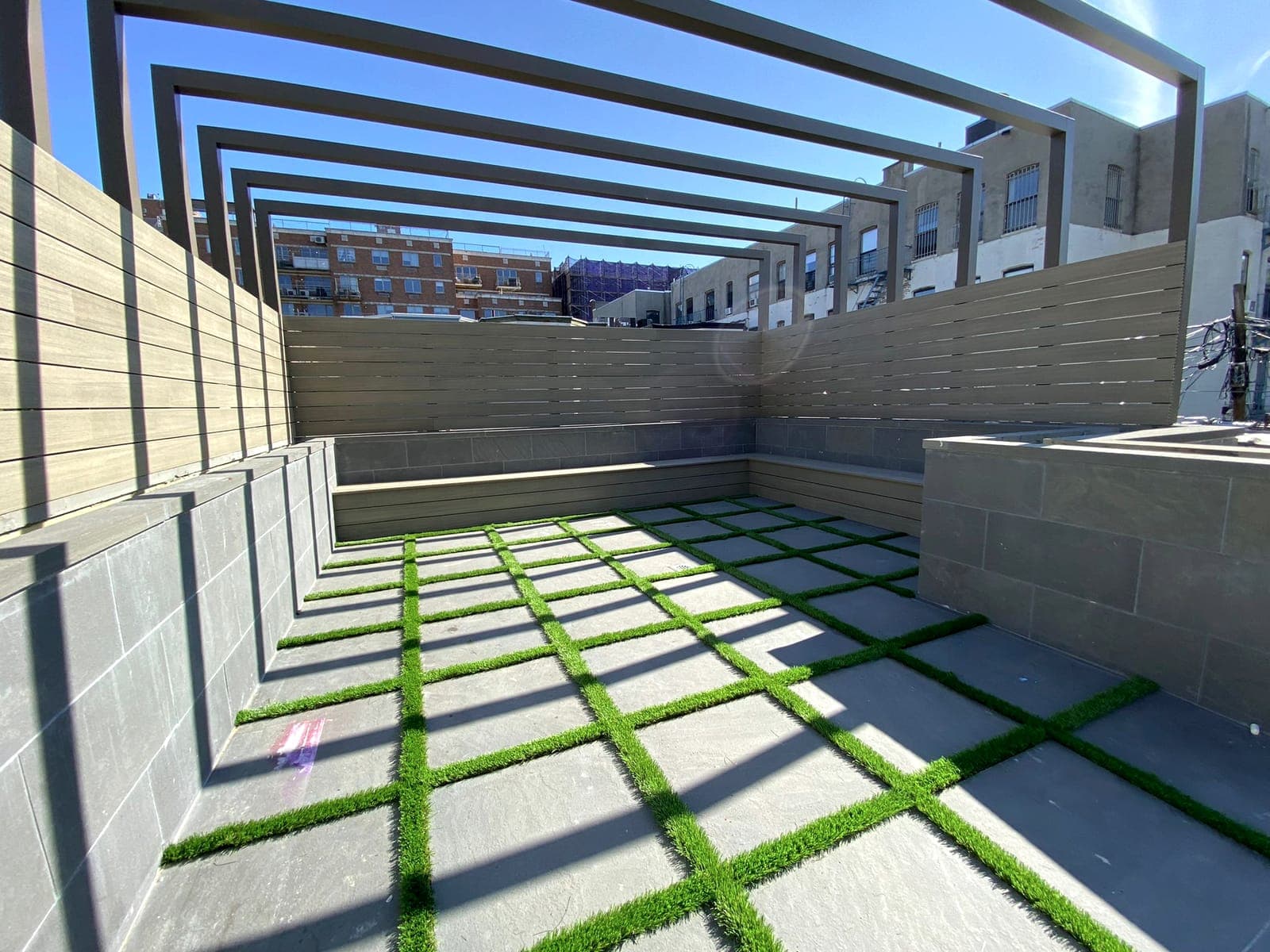 Rooftop with paver-and-grass floor and a black steel pergola frame